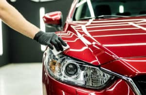 A person's gloved hand polishes the headlight of a shiny red car.