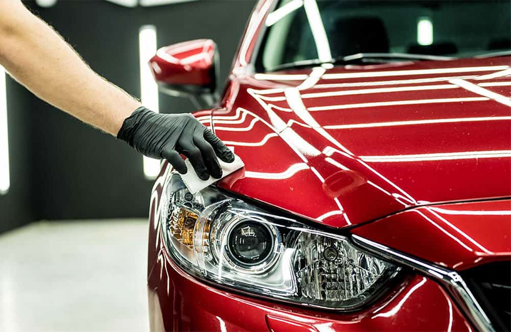 A person's gloved hand polishes the headlight of a shiny red car.