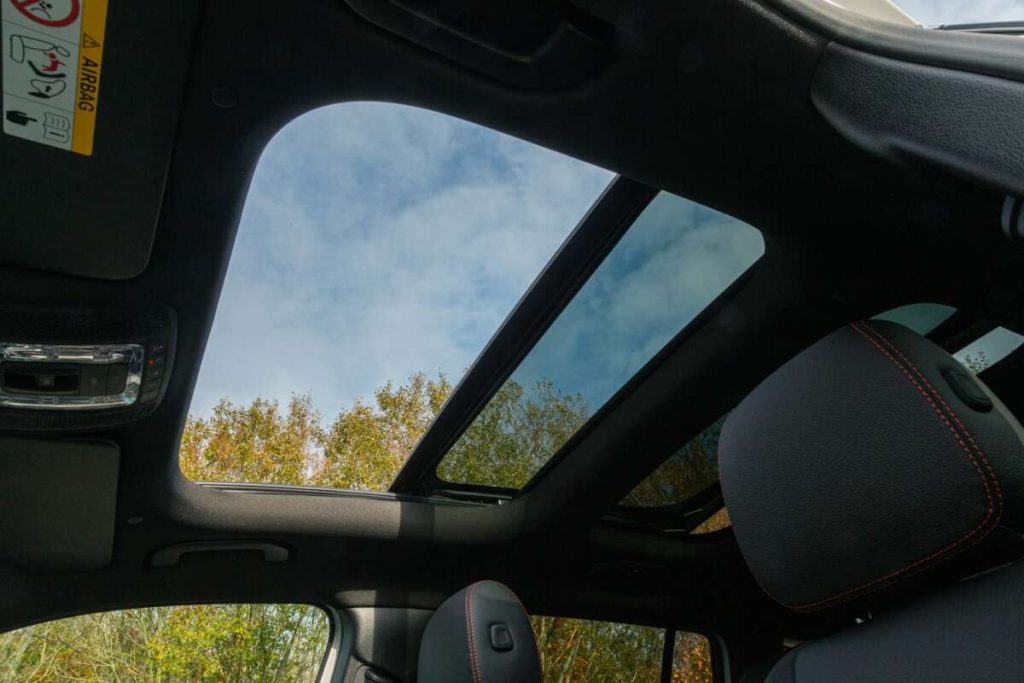 The car interior view features a panoramic sunroof, allowing glimpses of the clear sky and treetops, all enhanced by the ceramic window tint offering a cooler, glare-free ride.