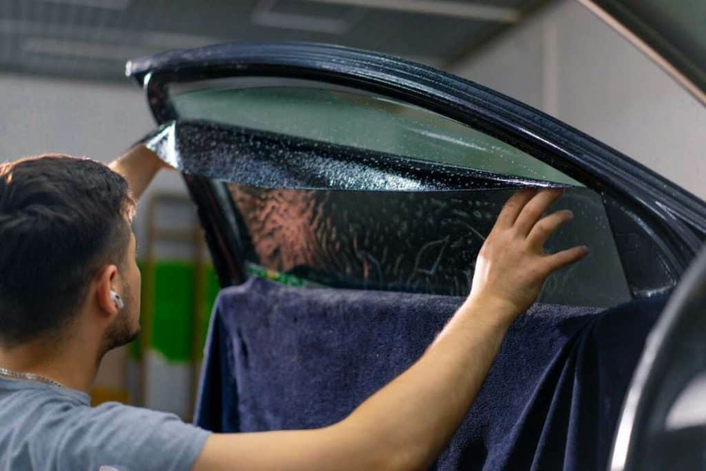 In a workshop setting, a skilled technician carefully applies tint to the car's rear window, ensuring seamless integration with its windshield protection film for enhanced durability.