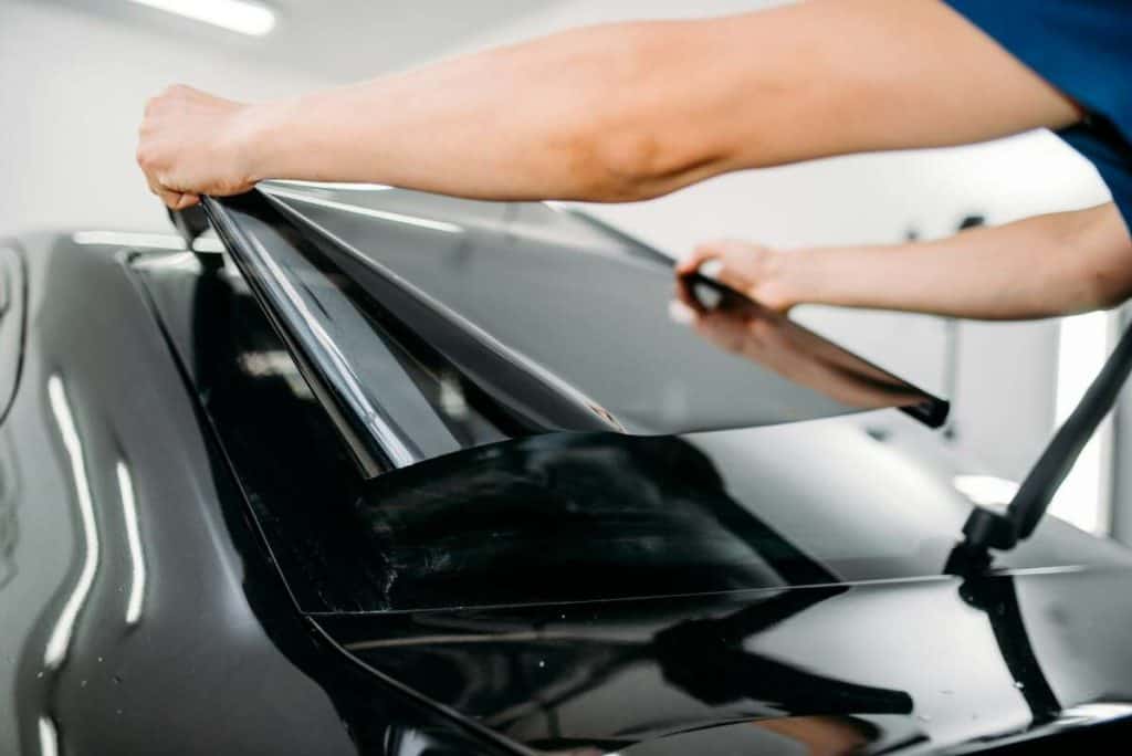 A person carefully applies ceramic window tint film to a car’s rear windshield, ensuring optimal protection and style.