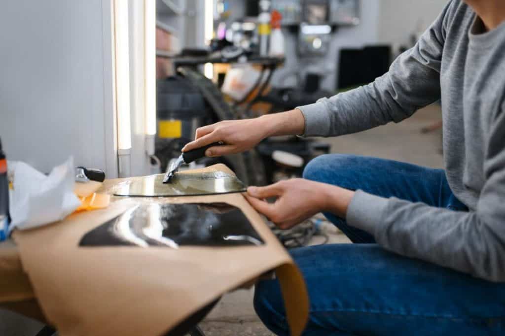 In a workshop setting, a person meticulously applies tinted film to the car window using a squeegee, ensuring flawless coverage and enhanced protection akin to that offered by windshield protection films.