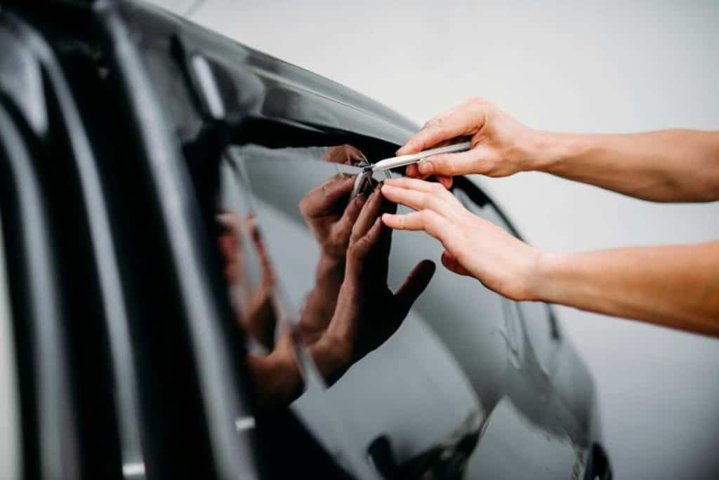 Applying tint film to a car window, this expert ensures a flawless finish with precision cutting using a knife. The addition of windshield protection film not only enhances style but also offers added durability against potential damage.