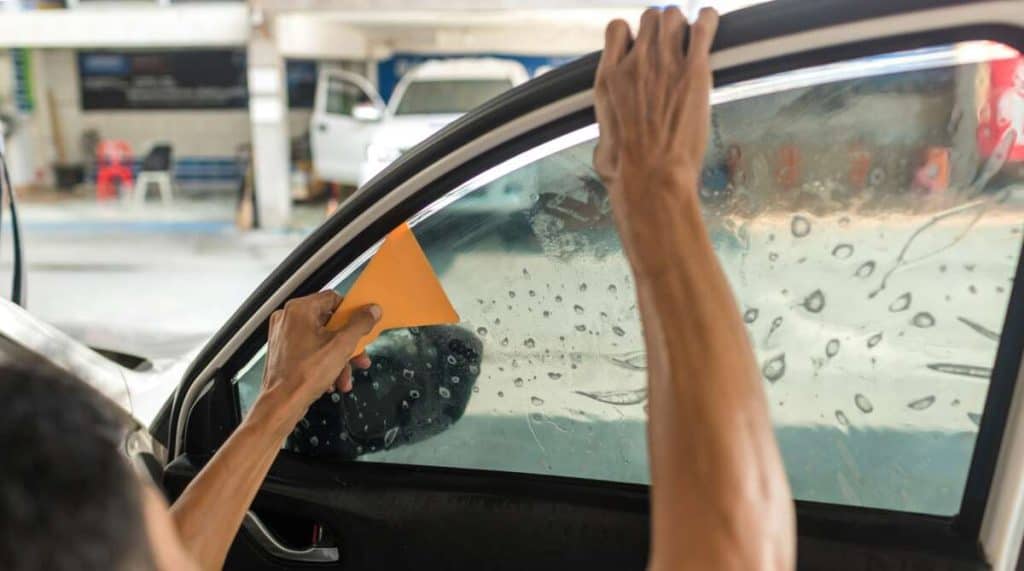 Applying windshield protection film, the person skillfully uses an orange tool to tint the car's window.