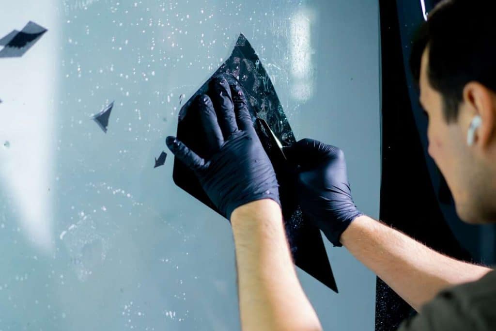 A person wearing gloves carefully applies windshield protection film to a glass surface.