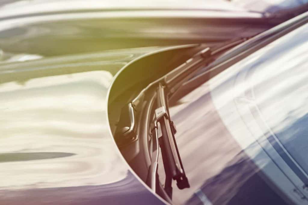 Close-up of a windshield wiper on a car, with sunlight reflecting on the glass and hood. A subtle layer of windshield protection film adds an extra sheen, ensuring clarity and durability against the elements.