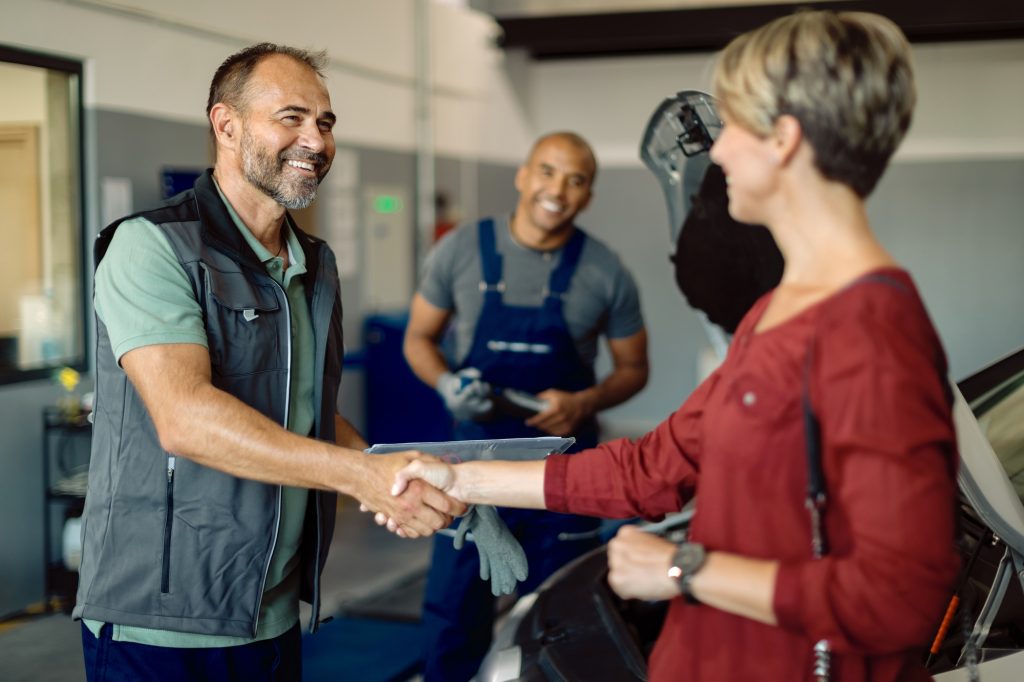 Happy mechanic handshaking with female customer in auto repair shop.